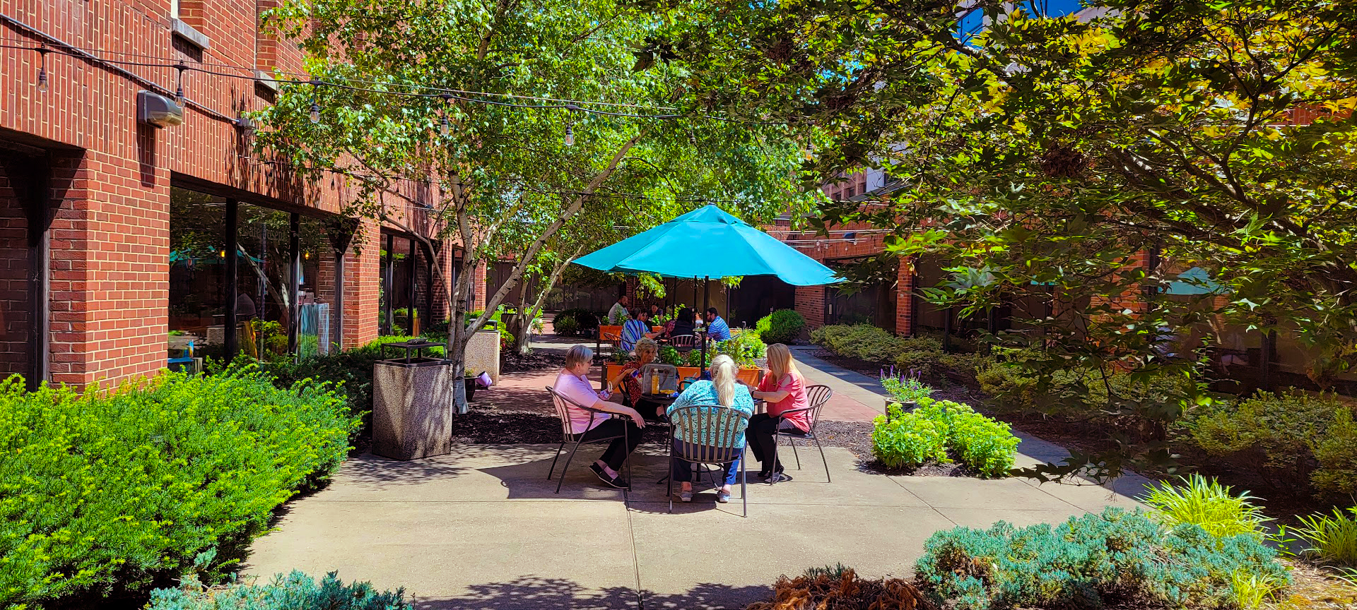 People seated beneath blue umbrellas in the landscaped St. Joseph courtyard.