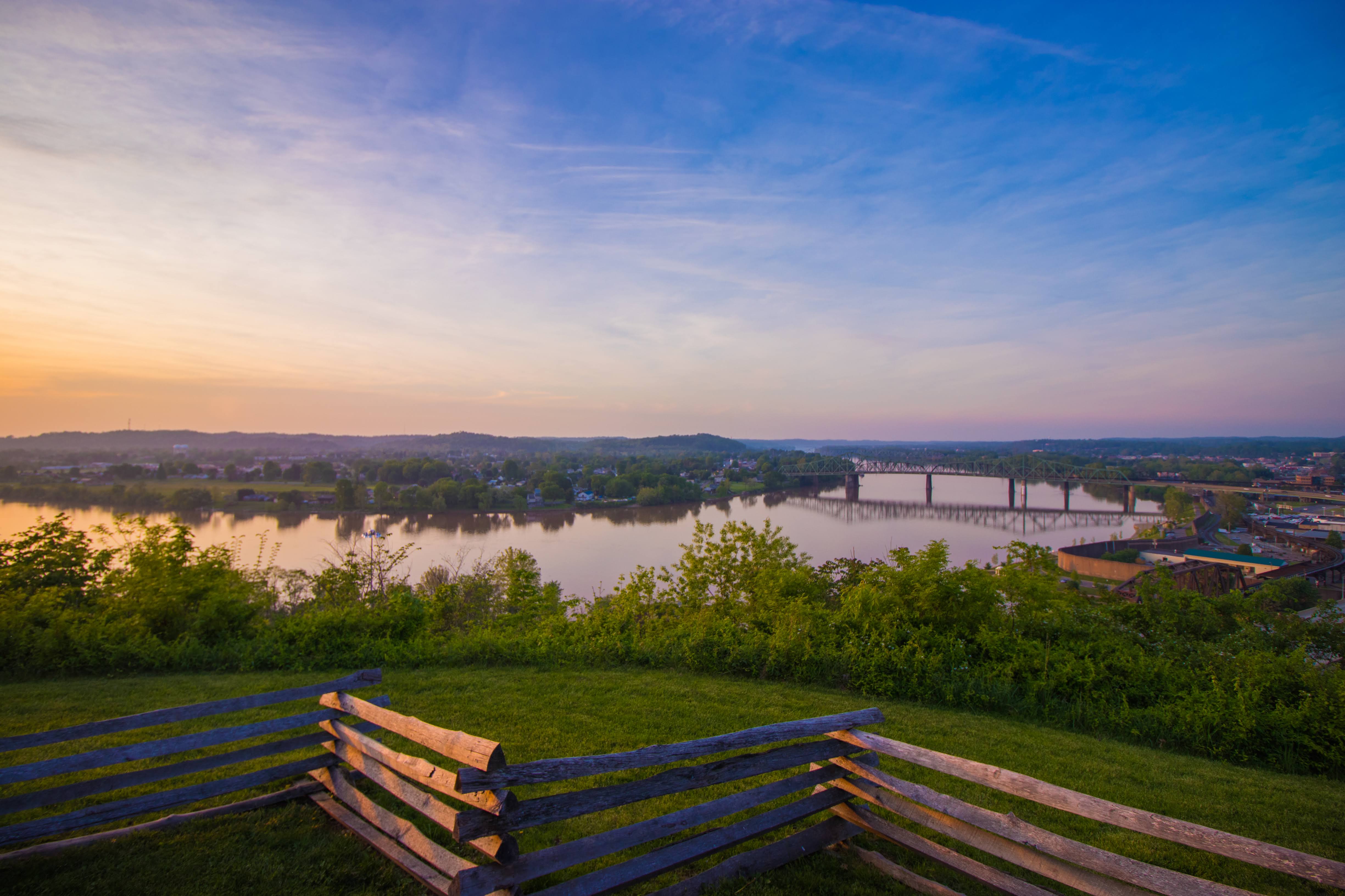 A bench above the river and bridge at sunset in Parkersburg, West Virginia.